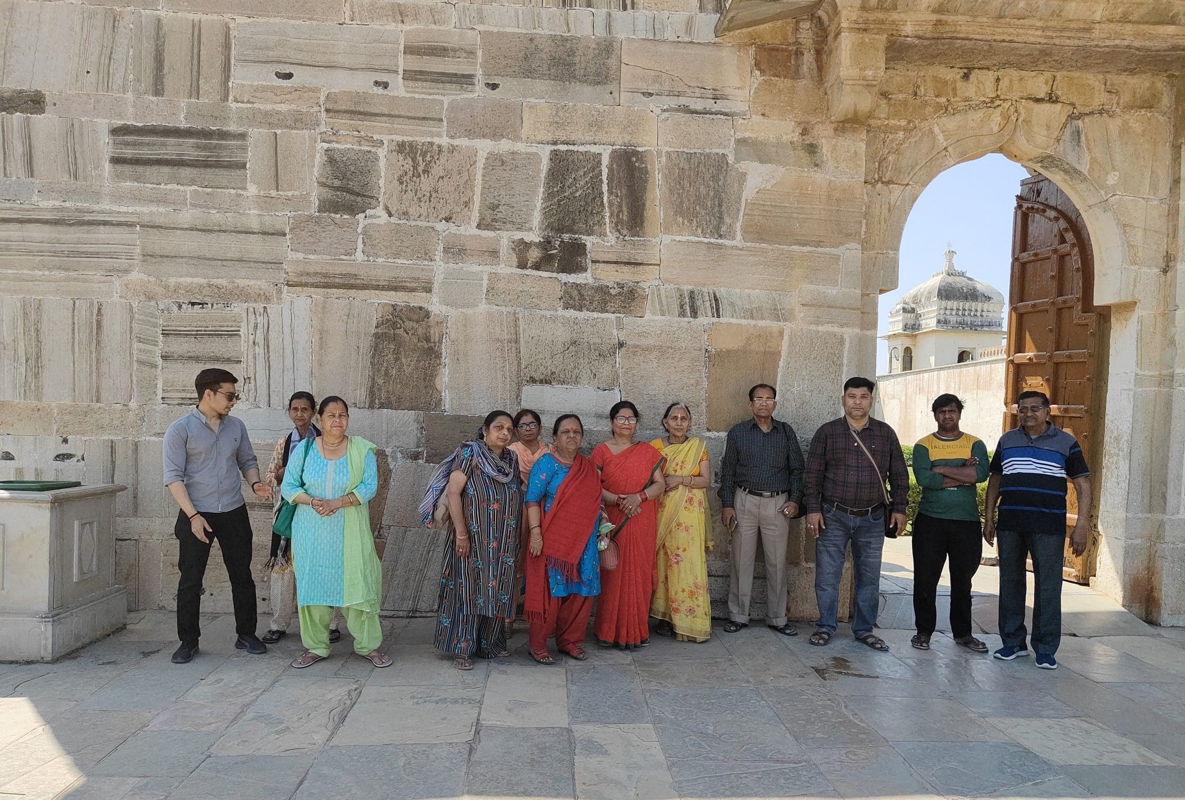 Travellers standing along a sandstone wall beside an arched gateway with a heavy wooden door at Chittorgarh Fort