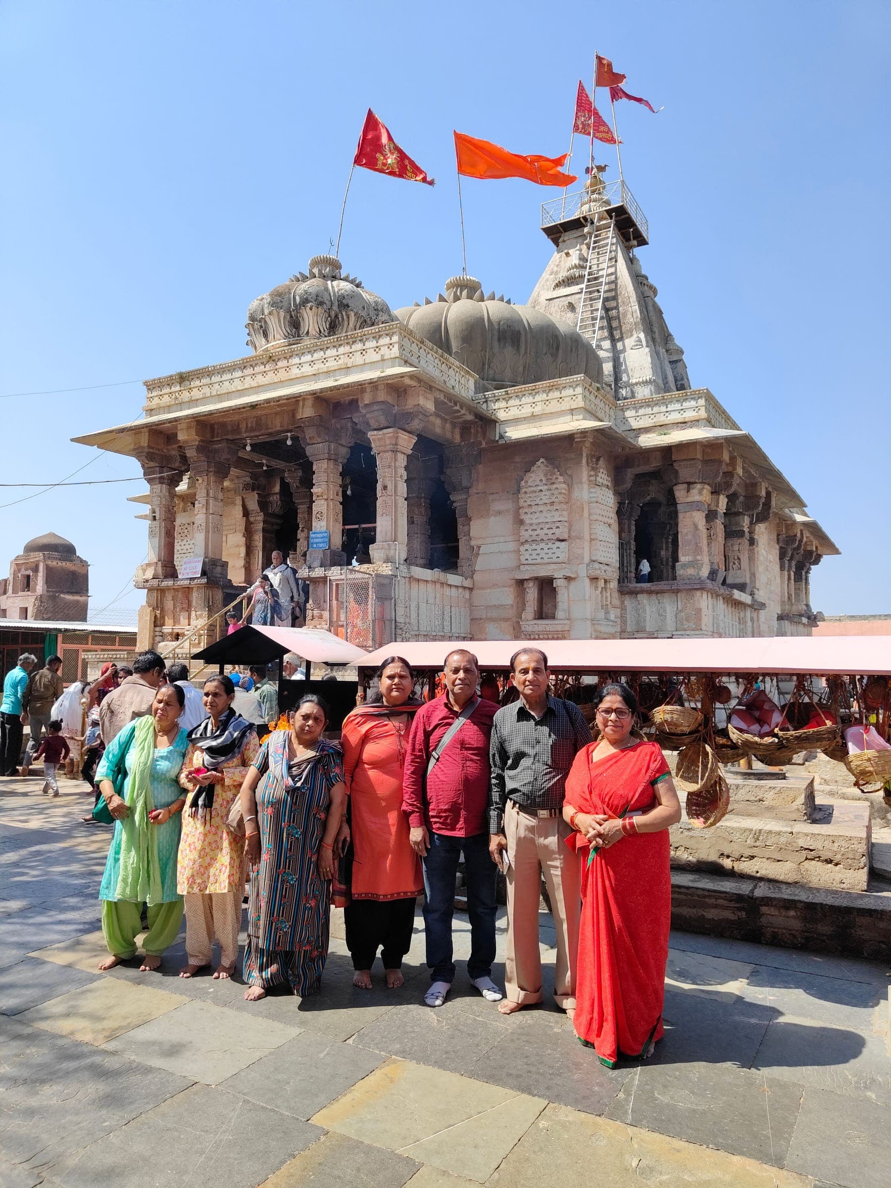 Travellers posing in front of a flag-topped stone temple inside Chittorgarh Fort