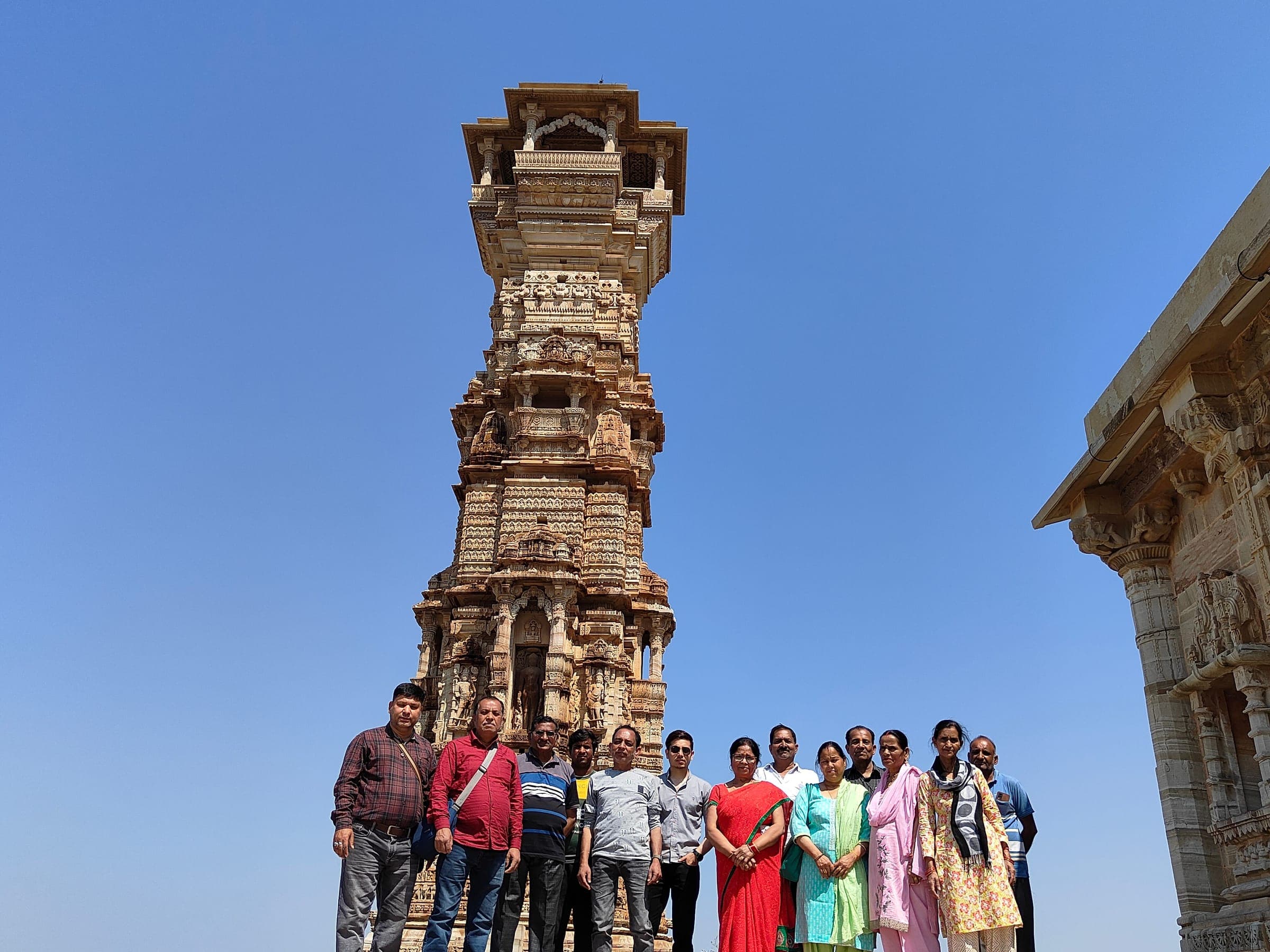 A group of travellers beneath the tall carved Kirti Stambh tower at Chittorgarh Fort under a clear blue sky