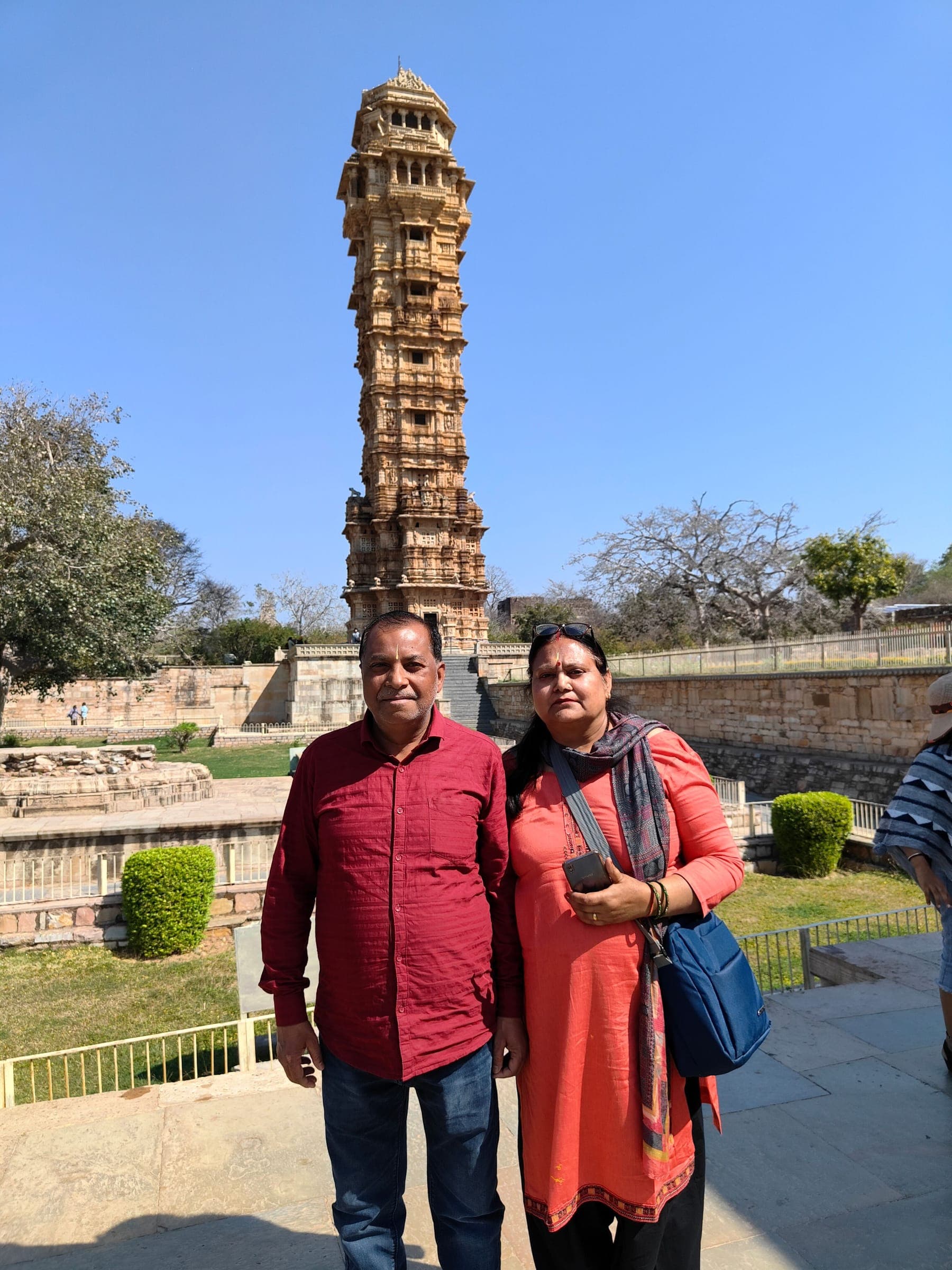 Two travellers standing in front of the carved Vijay Stambh tower at Chittorgarh Fort