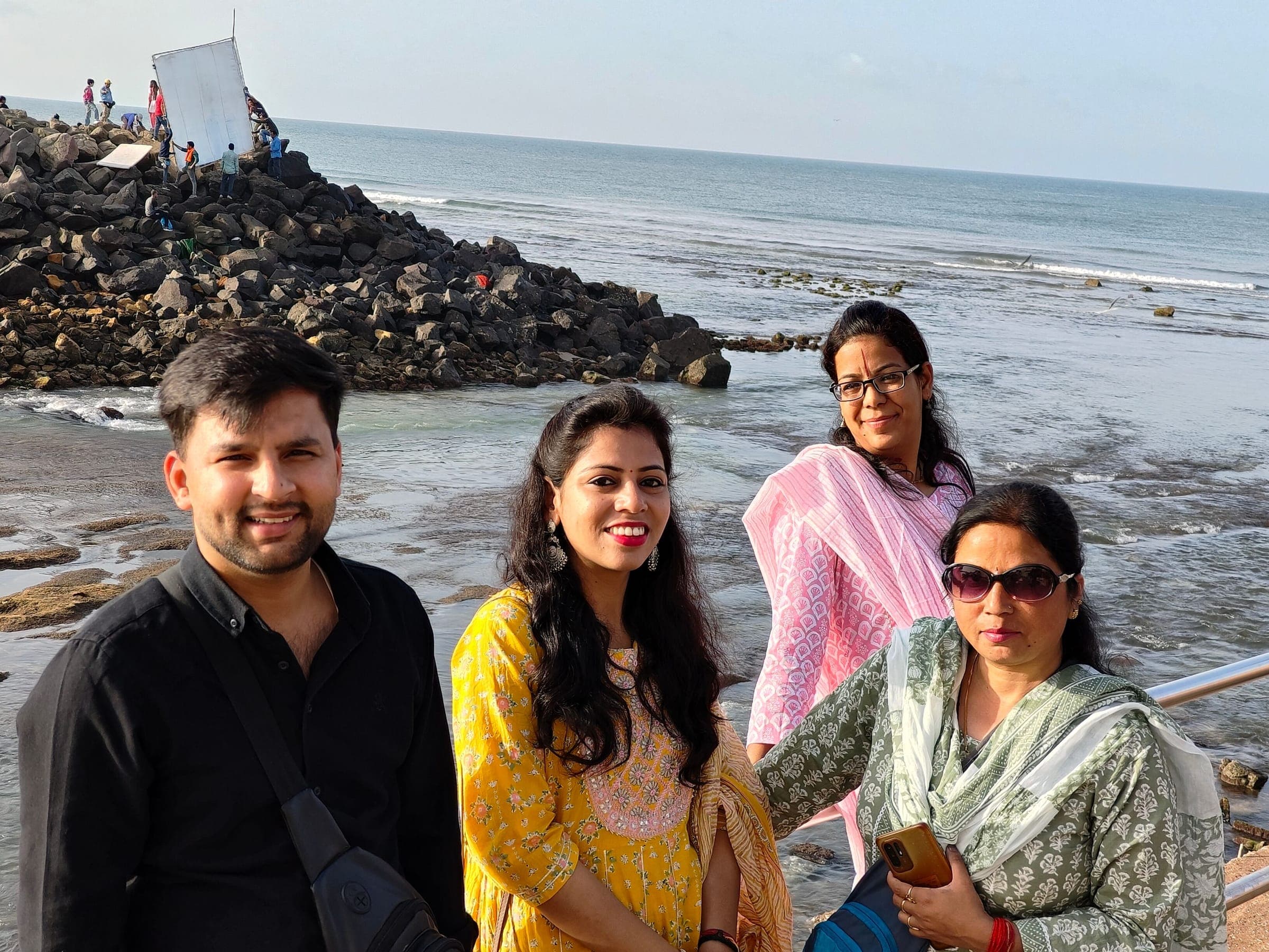 Four travellers smiling by the sea, rocks and breaking waves behind them
