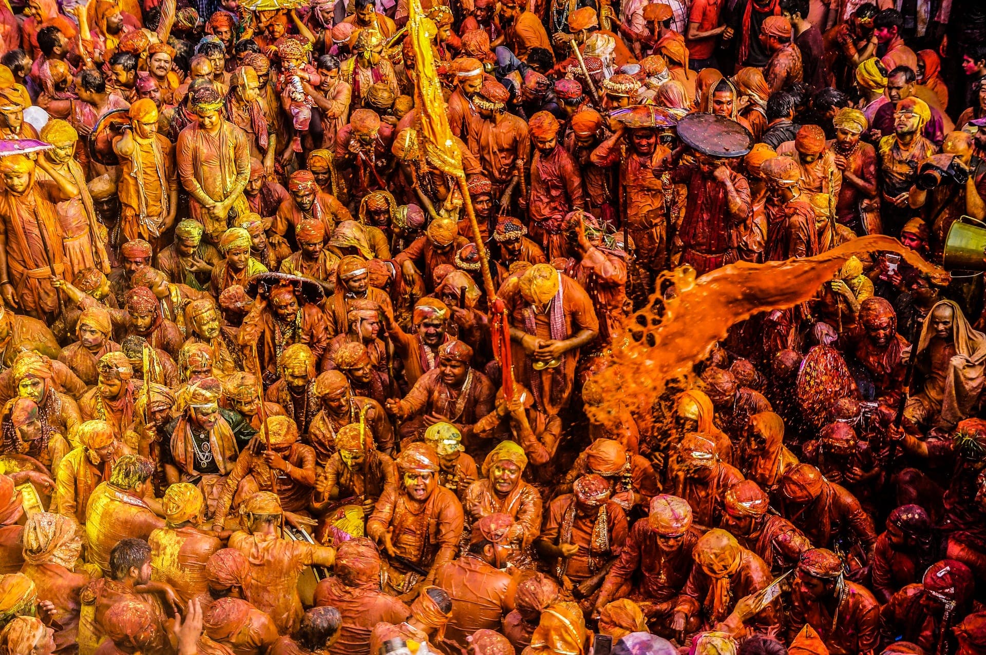 Holi in Mathura: a packed crowd drenched in saffron colour as a stream of coloured water arcs over them