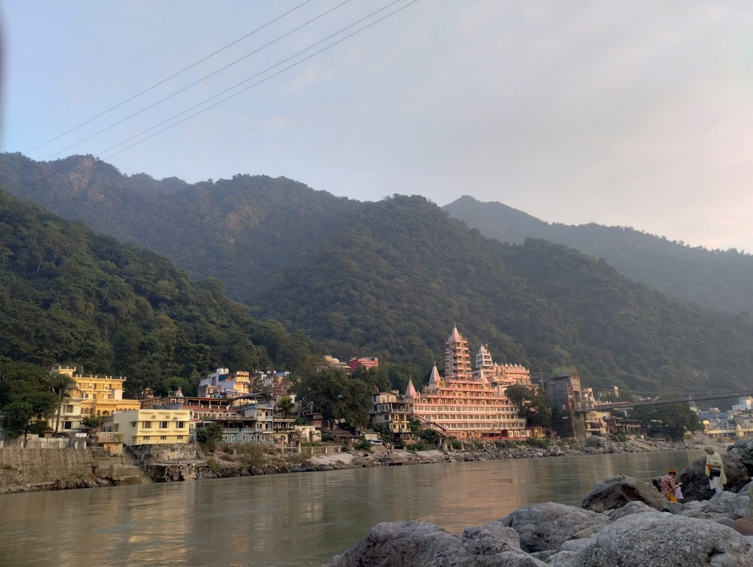 A many-storeyed temple on the banks of the Ganga at Rishikesh, wooded hills behind