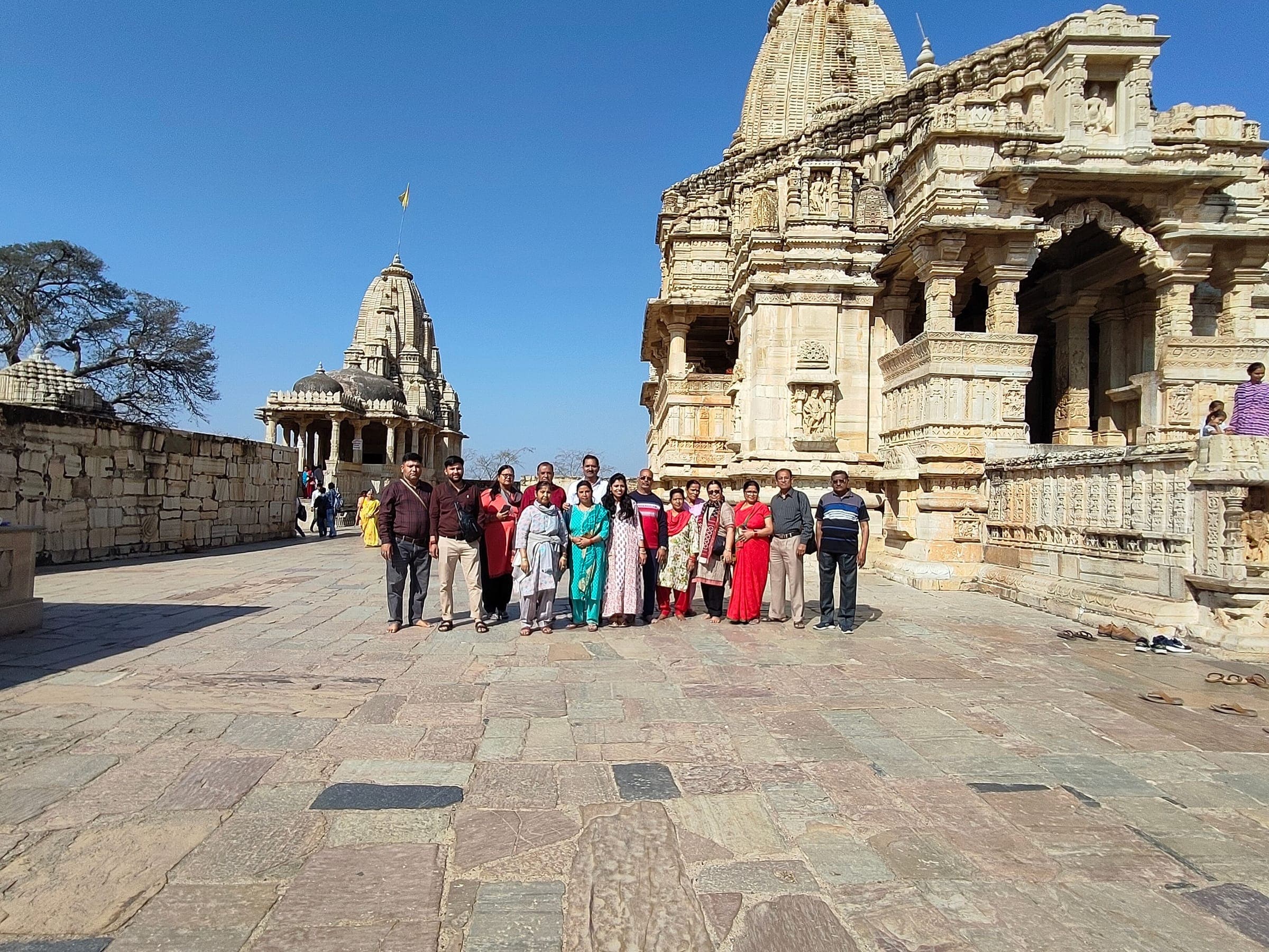 A Holidays Journey group standing together in a stone temple courtyard at Chittorgarh Fort, carved temple spires behind them