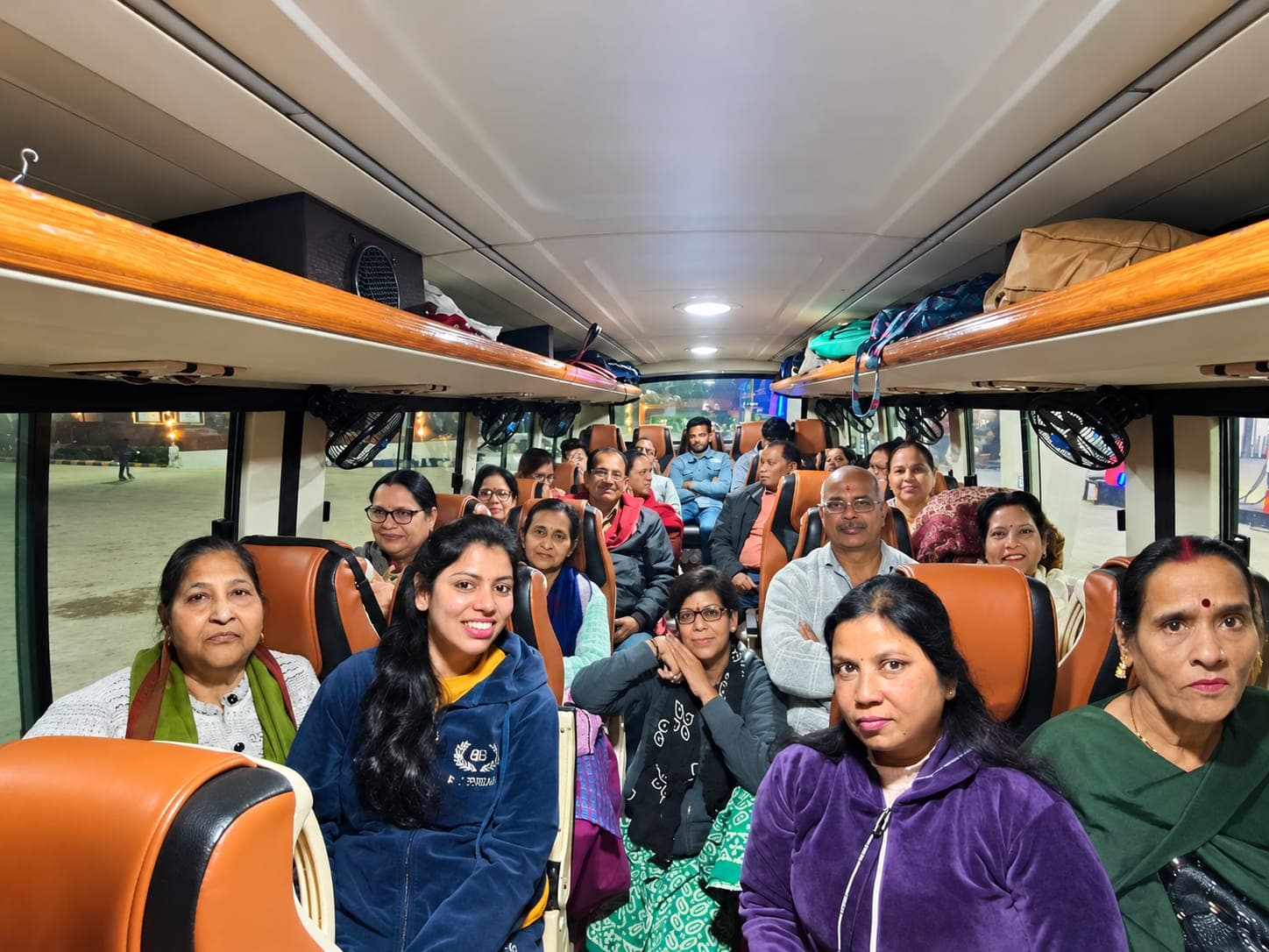 Travellers smiling from their seats inside a tour coach in the evening, luggage stowed on the racks overhead